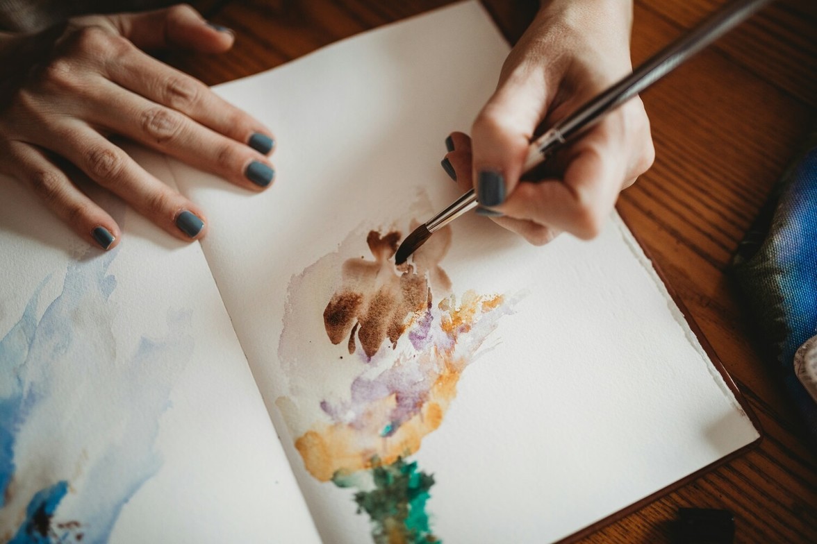 Close-up of hands painting with watercolours in a sketchbook, symbolizing a virtual art therapy session with a student therapist.