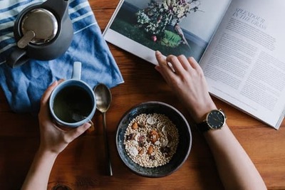 person sitting with bowl of oatmeal, coffee and reading a magazine
