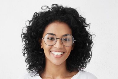 Close up of a smiling young woman of mixed race.  She has thick curly hair and is wearing glasses