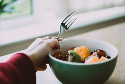 person holding bowl of fruit with fork in hand