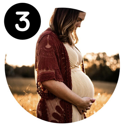 A pregnant woman standing outside in a field.