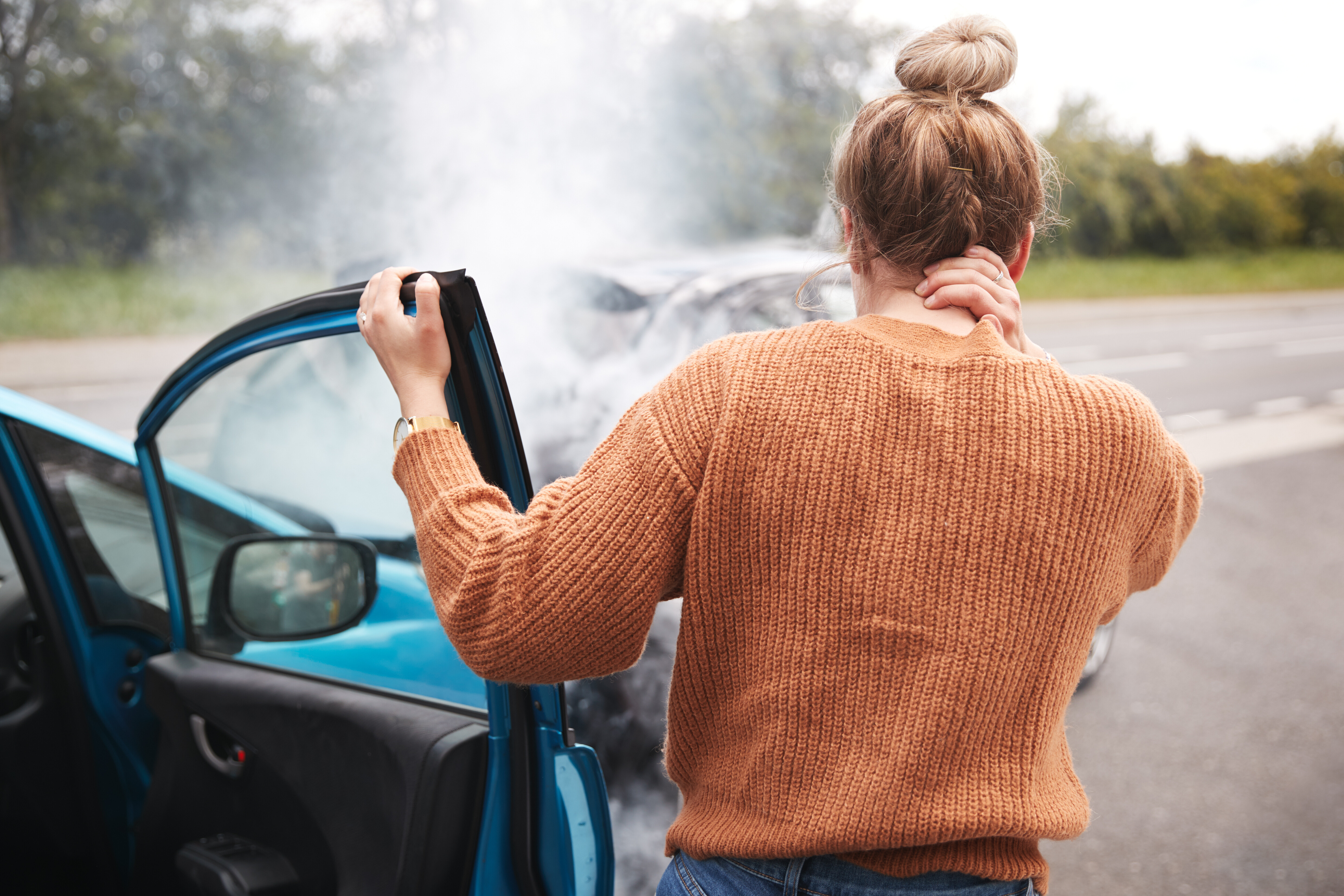 Woman who is holding her neck in pain stands next to car after a car accident. Whiplash