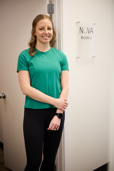 Team member and physiotherapist wearing green shirt standing in front of clinic treatment room in hallway