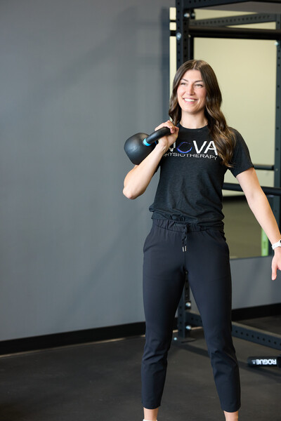 Team member and physiotherapist wearing black t shirt and holding kettlebell in gym setting with grey background