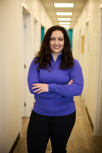 Woman standing in blue quarter zip in clinic hallway with crossed arms
