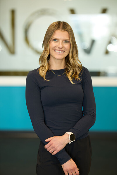 team member and physiotherapist standing in clinic gym wearing blue long sleeve shirt in front of nova window