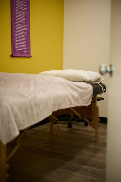 Massage table with white blanket ontop with yellow clinic wall behind and purple poster