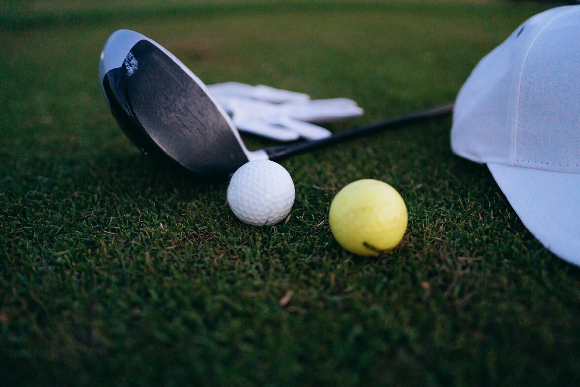 Golf supplies on grass; club, hat, ball 