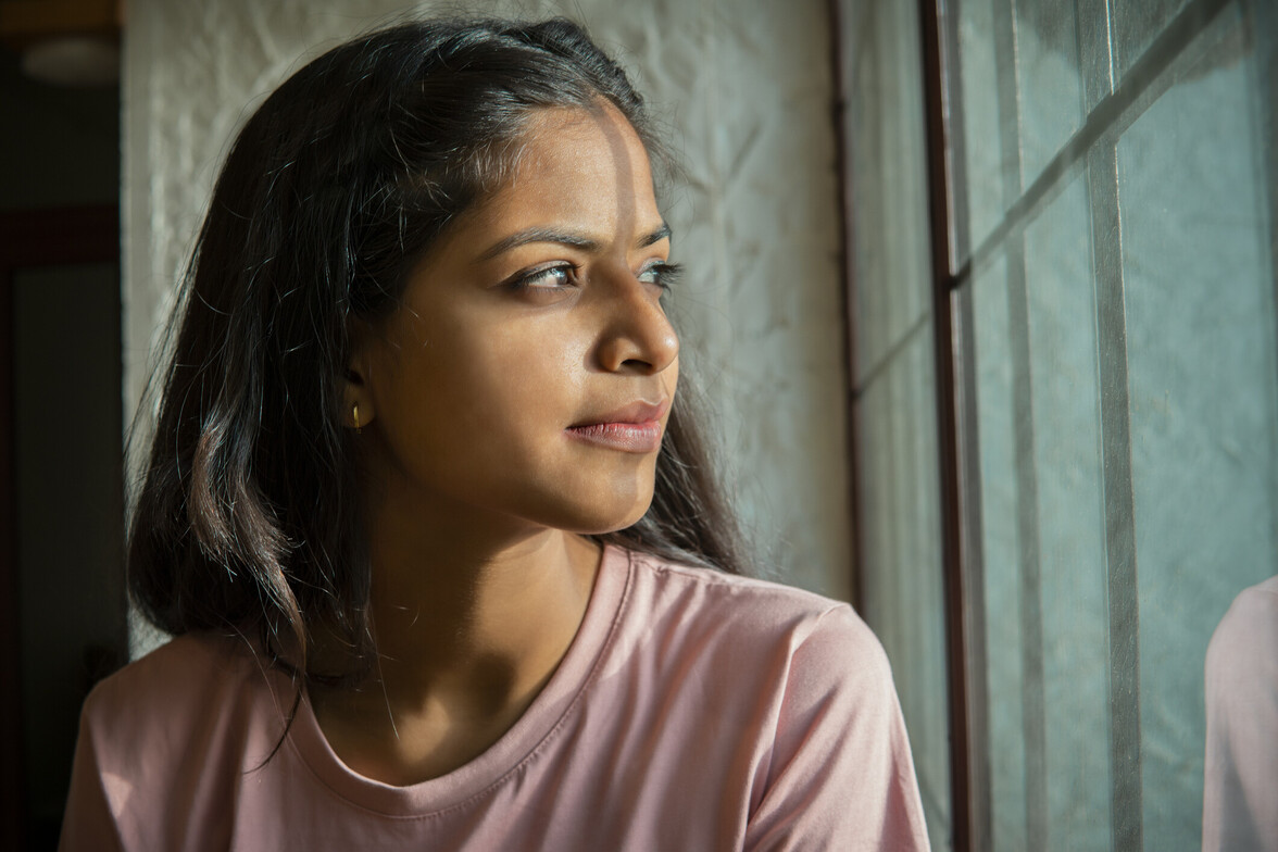 Woman looking out a window in soft natural light, appearing thoughtful and introspective