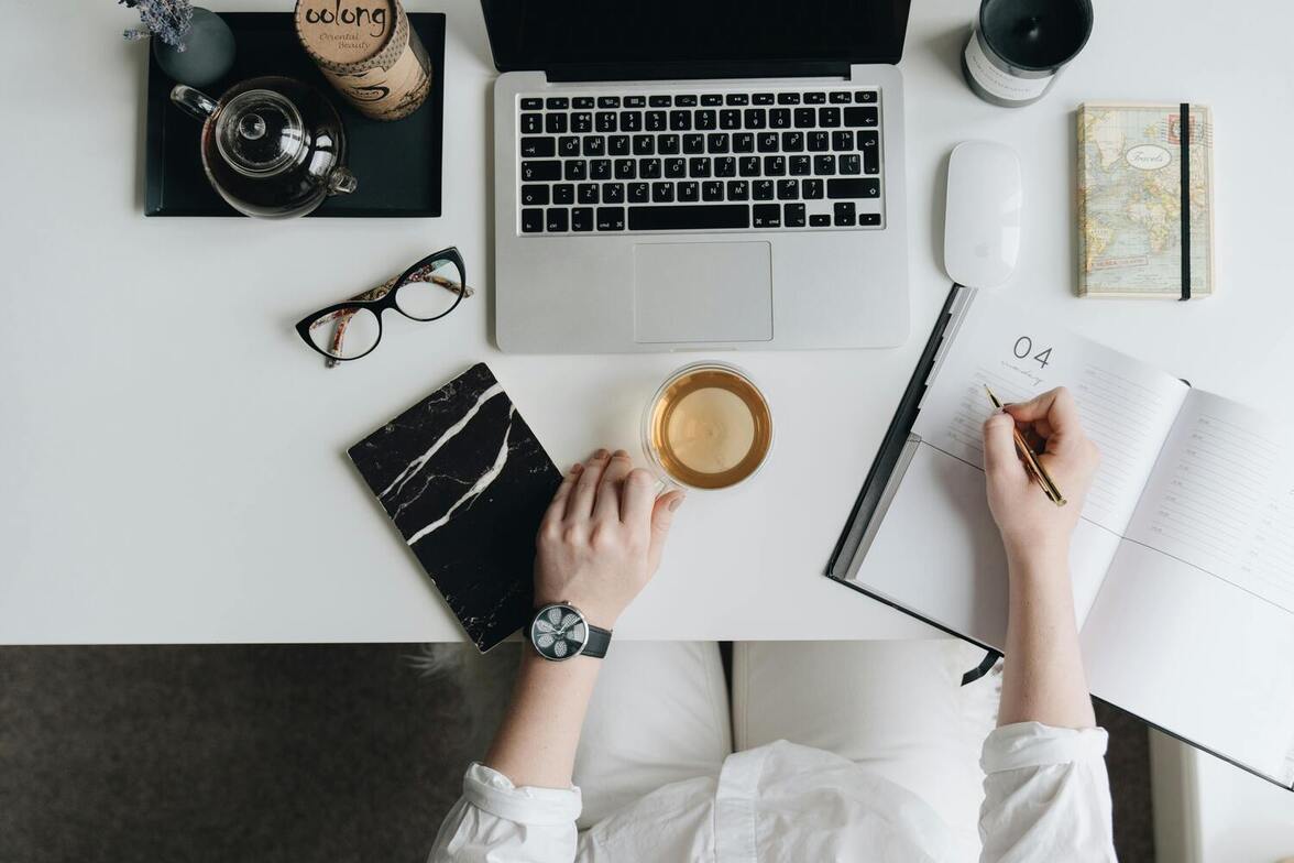 Therapist writing in her day planner while referencing her laptop—symbolizing the structured time commitment behind every therapy appointment, even when clients cancel or arrive late.