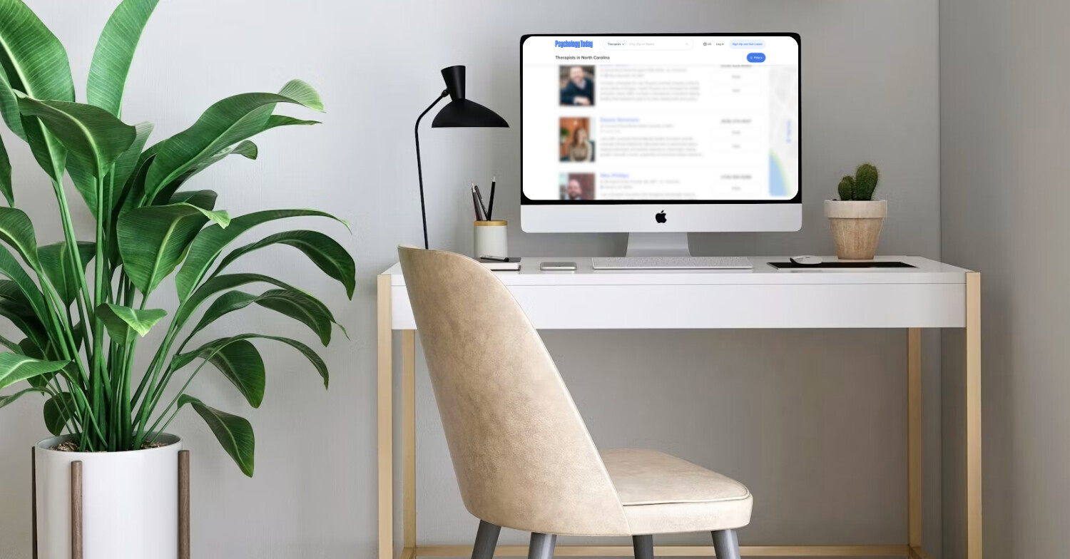 Minimalist home office with a desktop computer displaying therapist profiles, a large green houseplant, modern desk lamp, and clean workspace, representing the process of choosing a therapist.