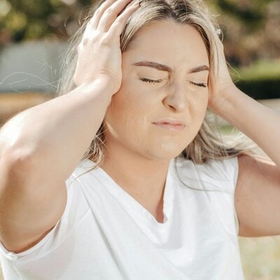 A woman holding her temples with a pained expression, illustrating the symptoms of a cervicogenic headache or migraine that can be treated at Handsworth Chiropractic Clinic.