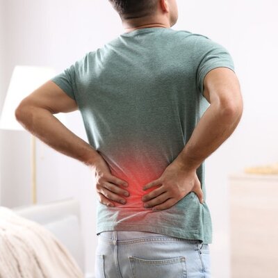 A person placing their hands on their back due to pain, representing how low back pain can be treated with chiropractic care.