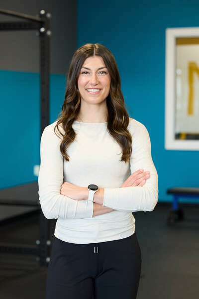 Nova team member and physiotherapist standing in white long sleeve in front of blue gym wall