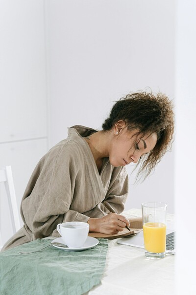 Woman writing in journal at home during virtual counselling process.