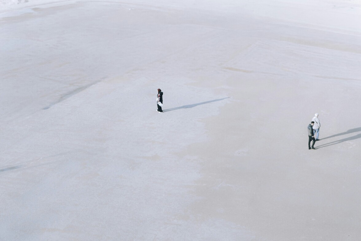 A person standing alone at a distance from two others in a large, empty space, illustrating feelings of not belonging.