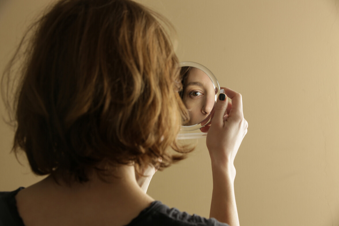Person holding a small mirror and looking at their reflection against a neutral background.