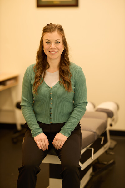 Nova team member and chiropractor wearing green sweater and sitting on chiropractic treatment table