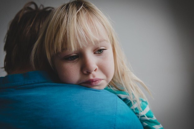 alt="Worried young girl resting on parent's shoulder, possibly experiencing discomfort or concern related to scoliosis"