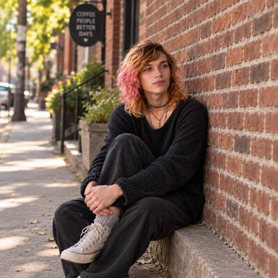 Transgender adult leaning against red brick wall, representing inclusive trauma and PTSD therapy in Ottawa and online across Ontario.