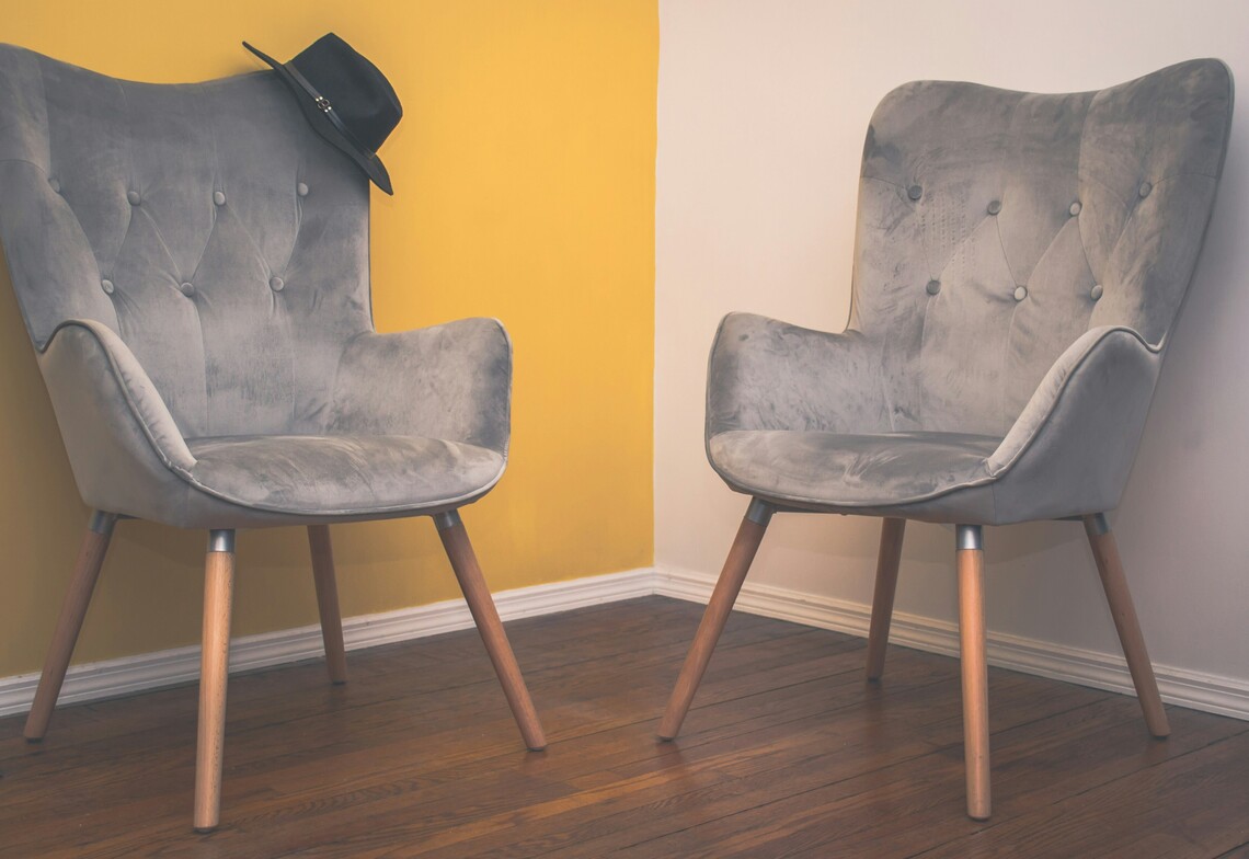Two empty chairs facing each other in a corner, symbolizing relational tension and freeze or fawn responses in adult parent relationships.