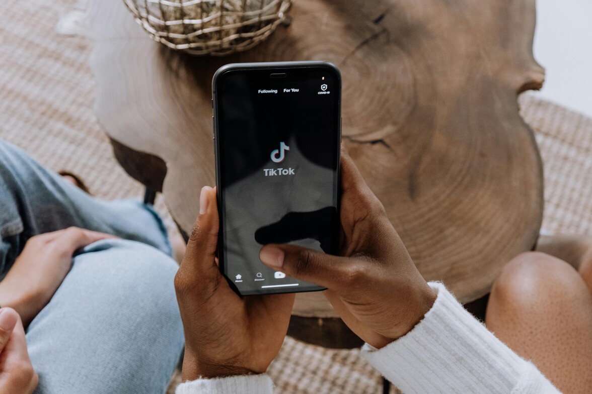 Hands holding a mobile phone displaying the TikTok app home screen 